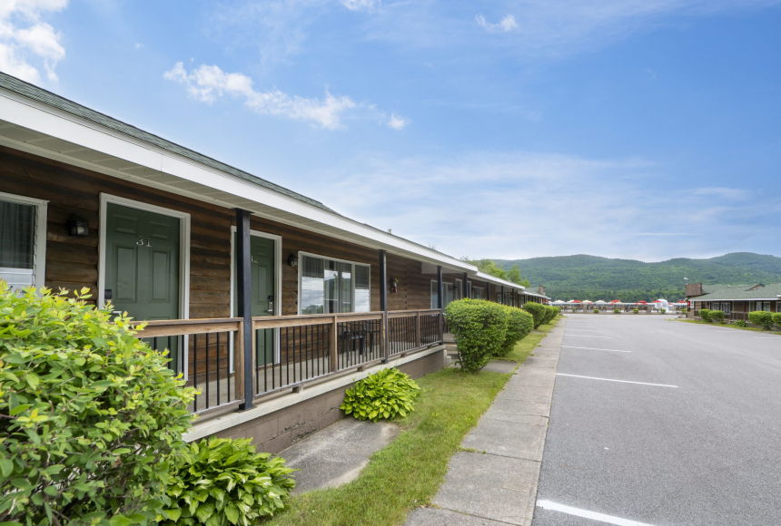 A wooden building with green doors and a parking lot in front of a mountainous backdrop.