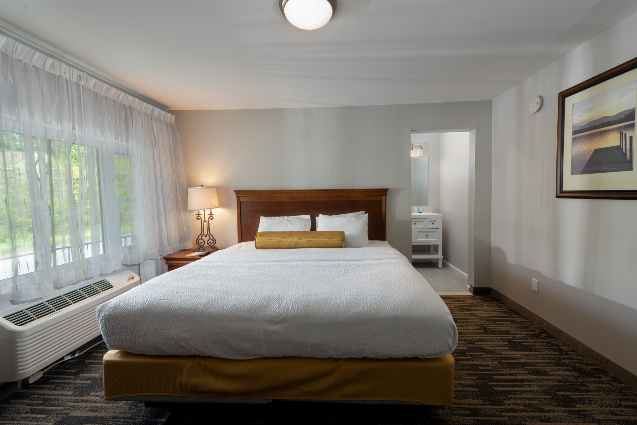 A hotel room with a large bed, window, and artwork